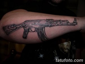 Фото реалистичной татуировки на предплечье с изображением автомата Калашникова, выполненной в черно-серых тонах.
