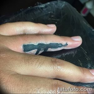 Фото миниатюрной татуировки на пальце с изображением автомата Калашникова, выполненной в черно-белом цвете.