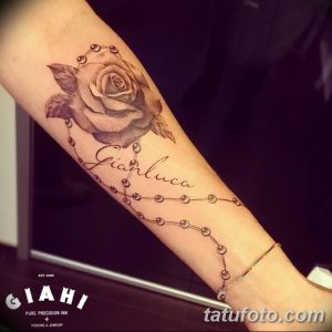 Фото тату: Черно-серая татуировка розы с именем 'Gianluca' на предплечье, украшенная бусинами-четочками. Изящный рисунок татуировки для женщин.