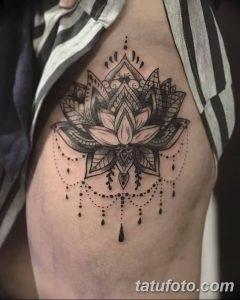 Фото тату: большой цветок лотоса на боку, выполненный в технике blackwork. Детализированный рисунок с тонкими линиями и узорами.