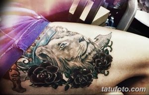 Фото тату головы львицы с черными розами на бедре. Цветная татуировка с детализированной проработкой шерсти и лепестков.