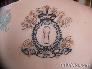 Фото тату: татуировка на спине с изображением замочной скважины, увенчанной короной, и надписью 'Fall Out Boy'.