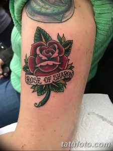 Фото тату: Красная роза с надписью 'Rose of Sharon' на руке. Детализированный рисунок татуировки в традиционном стиле.