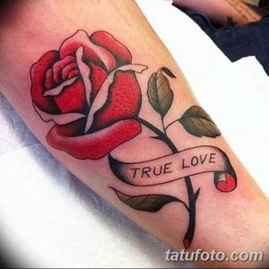 Фото тату: Красная роза с надписью 'True Love' на ленте, выполненная на руке. Детализированный рисунок татуировки с реалистичными лепестками и четкой надписью.