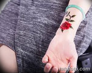 Фото тату: Маленькая красная роза с зелеными листьями на запястье, выполненная в минималистичном стиле.