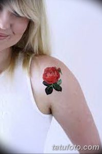 Фото тату: Красная роза с зелеными листьями на плече женщины. Нежный и детализированный рисунок татуировки.