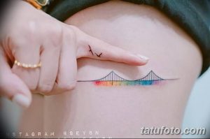 Фото минималистичной татуировки моста с радугой, расположенной на запястье. Рисунок выполнен в тонких линиях и ярких цветах.