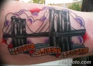 Фото тату Бруклинского моста в стиле олд скул с надписью 'Home Sweet Home' на предплечье. Яркие цвета и четкие линии.