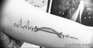 Фото простой татуировки моста и силуэта города на руке, выполненной в технике line work с использованием тонких линий и черного цвета.