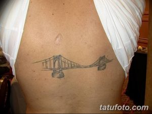 Фото минималистичной татуировки с изображением моста на боку, выполненной тонкими линиями в черно-белом цвете.