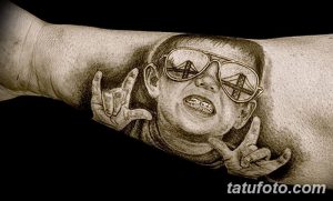 Фото черно-серой портретной татуировки с изображением человека в очках, в которых отражается мост Золотые Ворота, на предплечье.