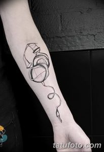 Фото тату: изящный рисунок наушников в стиле line work на руке. Черные линии на светлой коже, минималистичный дизайн.