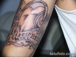 Фото тату на руке: реалистичное изображение наушников с надписью 'Music Forever'. Черно-белый рисунок татуировки в стиле реализм.