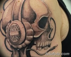 Фото тату на плече: череп в наушниках с микрофоном. Черно-серый рисунок в реалистичном стиле с элементами готики.