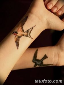 Фото тату с изображением двух ласточек на женском запястье. Одна ласточка в полете, другая силуэт. Детализированный рисунок татуировки.