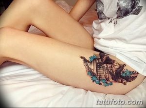 Фото тату: татуировка птицы в клетке на бедре. Оригинальный рисунок татуировки с использованием ярких цветов и детализированной прорисовки.