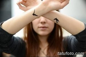 Фото тату двух маленьких черных ласточек на запястьях девушки. Изящный рисунок татуировки, выполненный в минималистичном стиле.