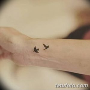 Фото татуировки с изображением двух маленьких птиц, летящих вокруг символа бесконечности на запястье. Тату выполнено в черном цвете.