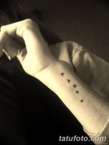 Фото татуировки на запястье: несколько маленьких птиц, летящих в одну сторону. Черно-белый рисунок.