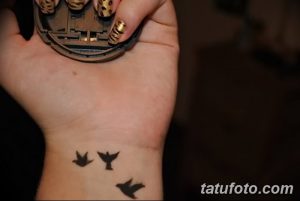 Фото тату: три маленькие черные птицы в полете, схематично изображенные на внутренней стороне запястья.