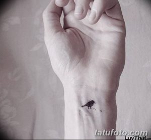 Фото тату с изображением одной маленькой черной птицы на запястье. Простой и элегантный рисунок татуировки.