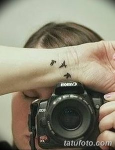 Фото татуировки фотоаппарата с летящей птицей на руке. Черно-белый рисунок, символ страсти к фотографии, минимализм.