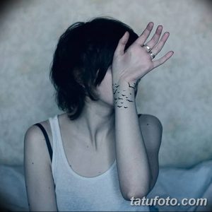 Фото татуировки на запястье с изображением стаи летящих птиц, выполненных в черном цвете в стиле графика.