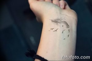 Фото татуировки на запястье с изображением пера и летящих птиц, выполненных в черно-серых тонах.