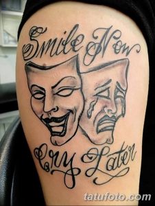 Фото тату на руке: две маски - смеющаяся и плачущая, с надписью 'Smile Now Cry Later'. Черно-серый рисунок татуировки.