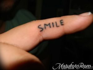 Фото тату: надпись "Smile" черными чернилами на пальце руки. Простая и мотивирующая татуировка.