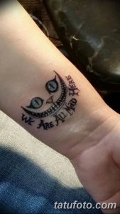 Фото тату на запястье: улыбающийся Чеширский Кот с надписью 'We are all mad here' вокруг него.