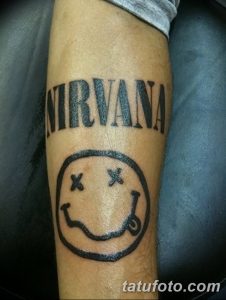 Фото тату на предплечье: логотип группы Nirvana – знаменитый смайлик с крестиками вместо глаз, надпись 'NIRVANA' сверху.