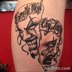 Фото тату двух масок – улыбающейся и плачущей, с надписями 'Smile Now' и 'Cry Later'. Черно-белая татуировка на ноге, выполненная в реалистичном стиле.