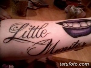 Фото тату надписи 'Little Monster' с изображением губ, показывающих клыки. Черно-белая татуировка на предплечье, выполненная в каллиграфическом стиле.