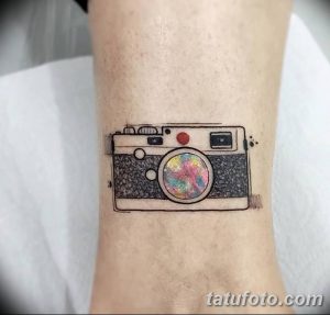 Небольшая татуировка на руке с изображением фотоаппарата, объектив которого выполнен в радужных цветах. Оригинальный и яркий дизайн.