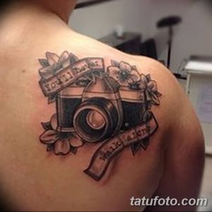 Фото татуировки с изображением старинного фотоаппарата, украшенного цветами, на плече мужчины. Детализированный рисунок в стиле олдскул.