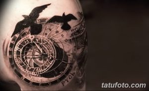 Фотография черно-серой татуировки на плече, изображающей компас, ворона и часы. Детализированный рисунок тату в стиле реализм.