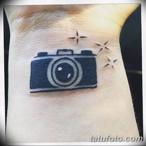 Фото тату маленького фотоаппарата с искрами, расположенного на запястье, выполненного в синих тонах.