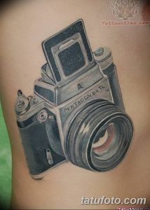 Фото тату реалистичного изображения старинного фотоаппарата на предплечье, выполненного в черно-серых тонах с высокой детализацией.