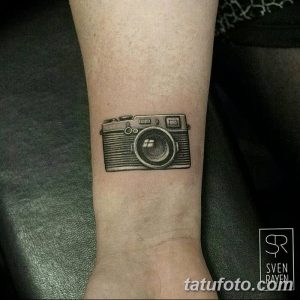 Фото тату на запястье: черно-серый контурный рисунок старинного фотоаппарата, выполненный в классическом стиле.