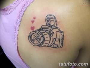 Простое черно-белое фото тату фотоаппарата на плече с двумя маленькими сердечками. Минималистичный стиль, нежные линии.