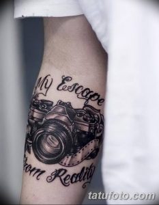 Черно-белое фото тату фотоаппарата на предплечье с надписью 'My Escape from Reality'. Детализированный рисунок, реалистичный стиль.