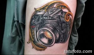 Фото тату: детализированный фотоаппарат Nikon в золотой декоративной рамке на руке. Классический стиль и изысканный дизайн.
