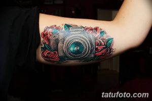 Красочная татуировка фотоаппарата, окруженного красными розами на руке. Реалистичный рисунок с яркими цветами и детальной проработкой.