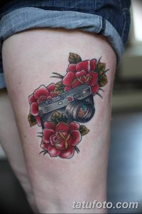 Красочная татуировка фотоаппарата, окруженного красными розами на бедре девушки. Стиль олдскул с четкими контурами и яркими цветами.