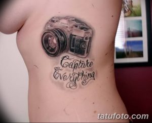Черно-серая татуировка фотоаппарата с надписью 'Capture Everything' на боку девушки. Реалистичный рисунок с каллиграфическим шрифтом.