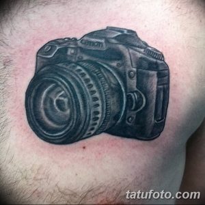 Черно-серая реалистичная татуировка фотоаппарата Canon на груди мужчины. Детализированный рисунок с точной проработкой всех элементов камеры.