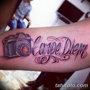 Фото тату фотоаппарата Pentax и надписи 'Carpe Diem' на руке. Мотивирующий и стильный рисунок татуировки в черно-серых тонах.
