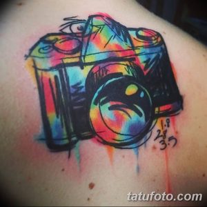 Фото акварельной тату фотоаппарата на плече. Яркий и красочный рисунок татуировки, выполненный в технике акварели с брызгами краски.