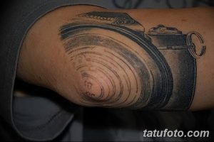 Фотография татуировки с изображением камеры Canon на предплечье. Детализированный рисунок в черно-серых тонах, реалистичный стиль.